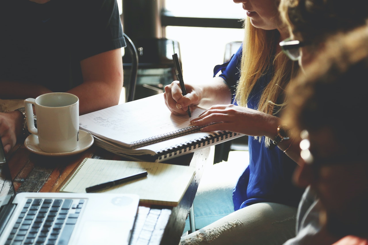 people sitting around desk, writing on notebook